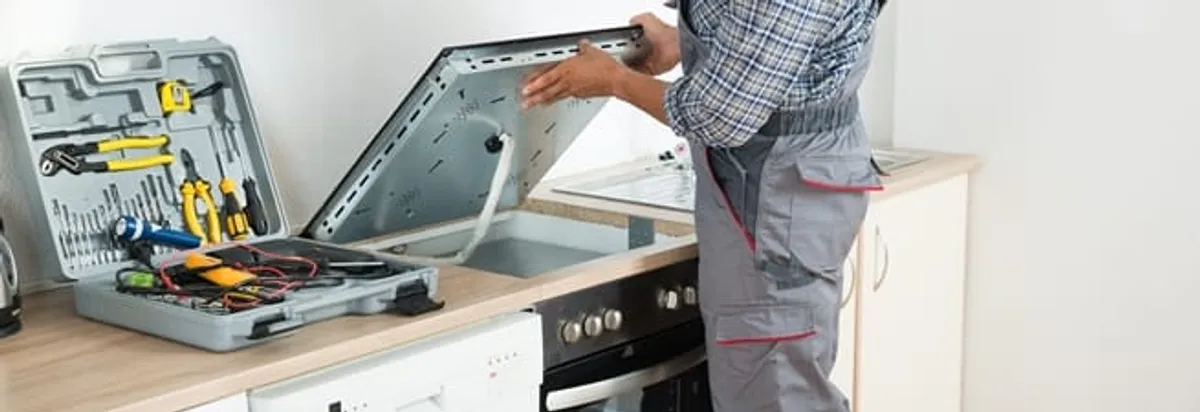 Cooktop repair technician lifting a built-in stovetop for service in Omaha, NE