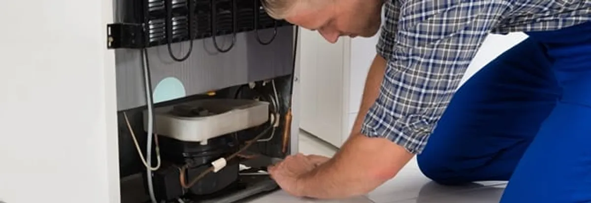 Refrigerator repair technician servicing the compressor and condenser area in Omaha, NE